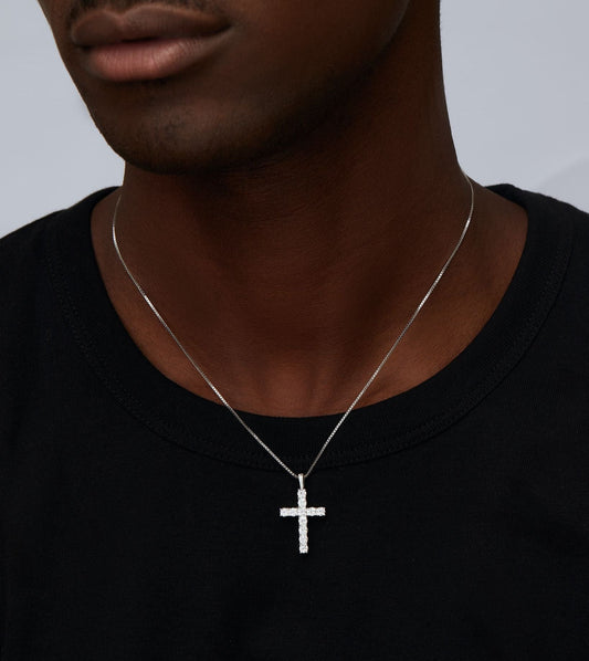 Person wearing a silver cross necklace on a plain background