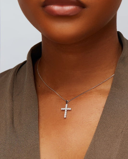 A person wearing a small silver cross pendant on a chain.