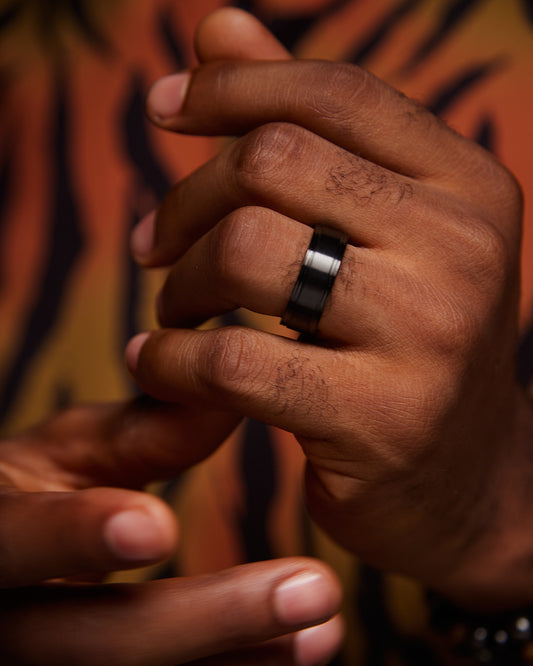A close-up image of a man's hand wearing a black titanium ring.