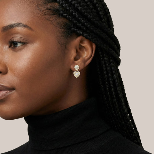 Close-up of a woman wearing gold heart-shaped earrings with a neutral background