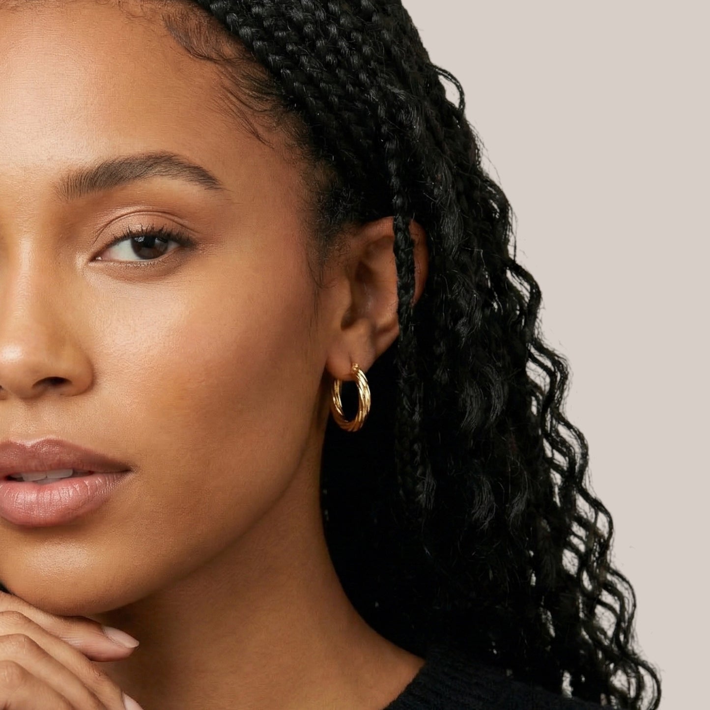 Close-up of a woman with braided hair wearing gold hoop earrings against a neutral background