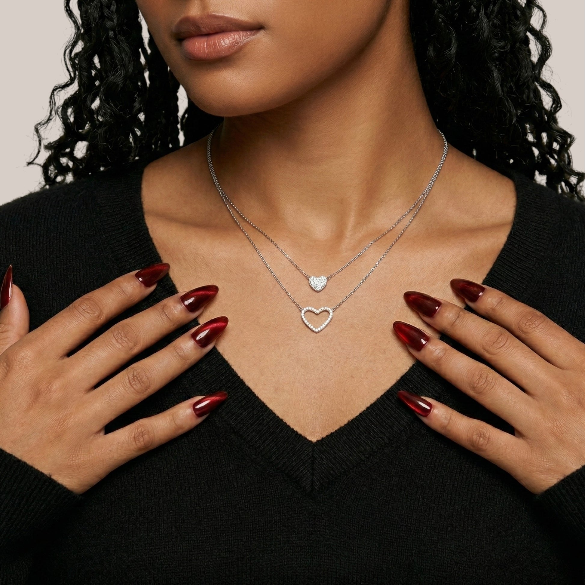 Woman wearing a silver heart-shaped necklace with a clear heart pendant, against a neutral background.