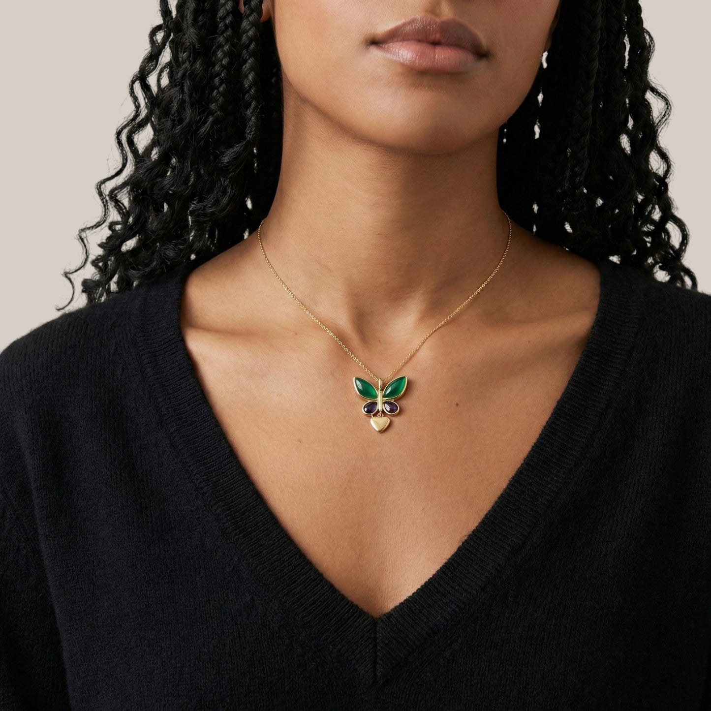 Woman wearing a gold necklace with a green butterfly pendant against a neutral background