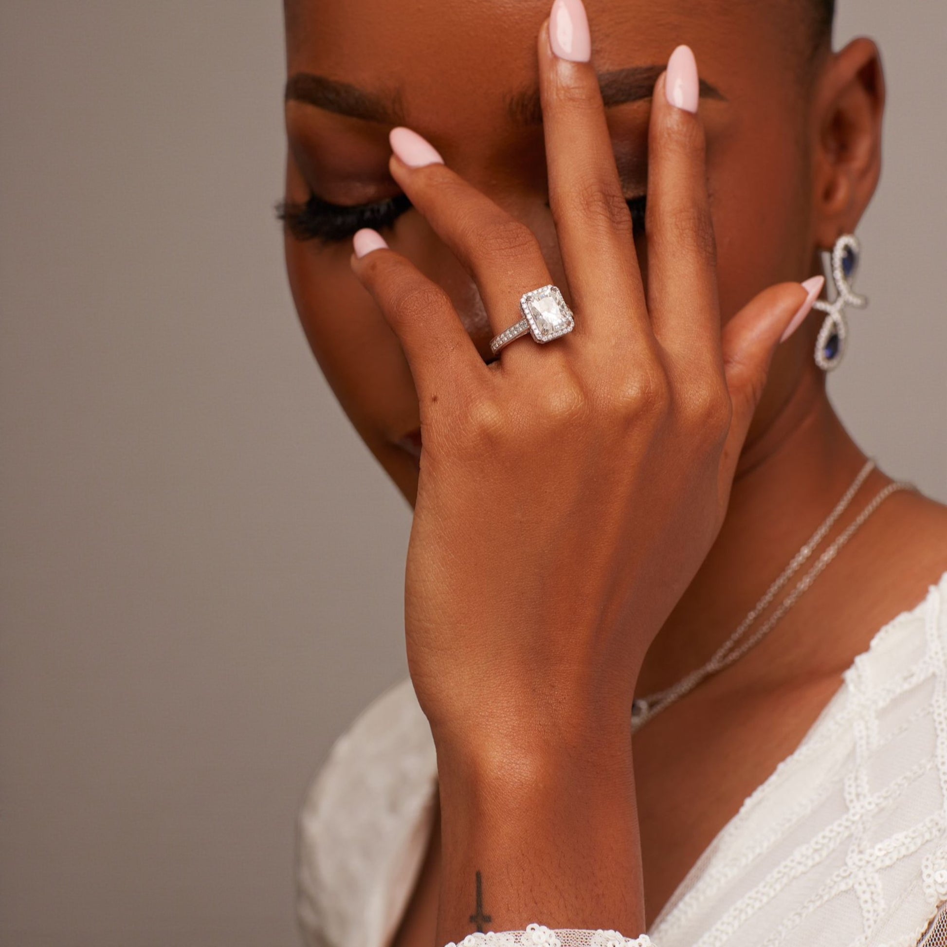 Close-up of a hand with a diamond ring on a neutral background