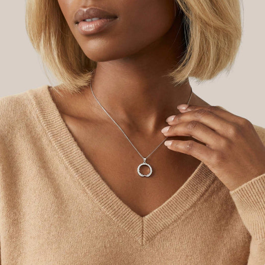 Woman wearing a beige sweater and a necklace with a circular pendant.