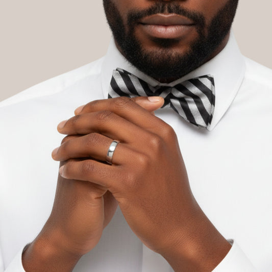 Man wearing a white shirt with a black and white striped bow tie, clasping his hands together.