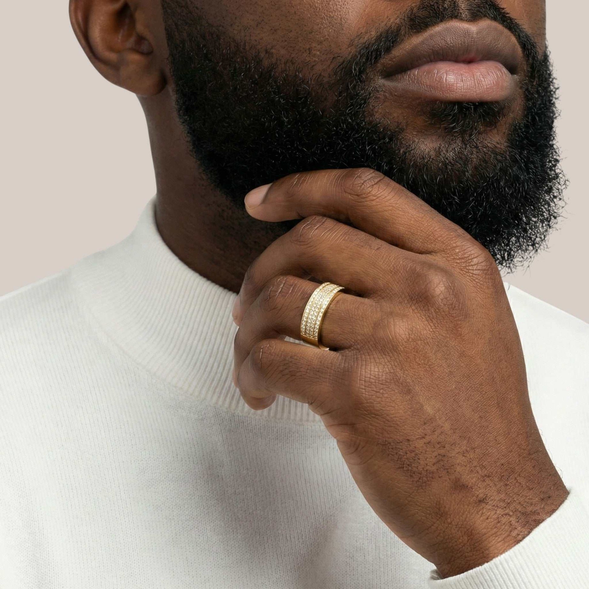 Man wearing a gold ring on his finger, touching his chin against a neutral background