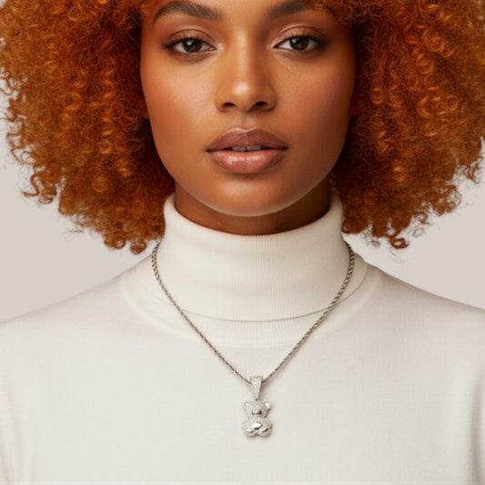 Woman wearing a white turtleneck and silver necklace with a pendant against a neutral background