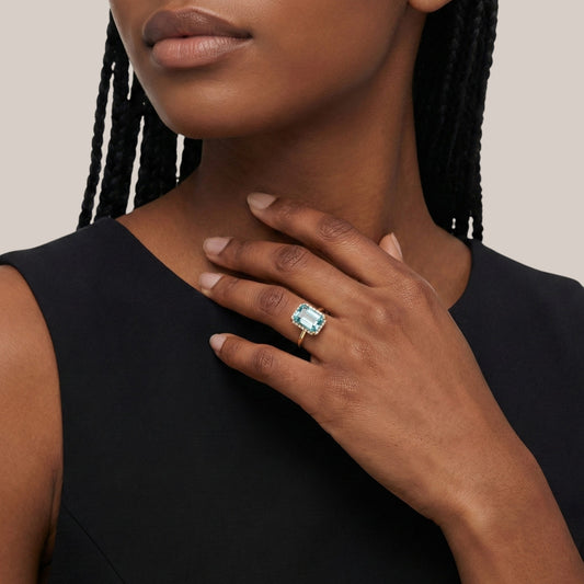 Woman wearing a ring with a prominent gemstone on a plain background