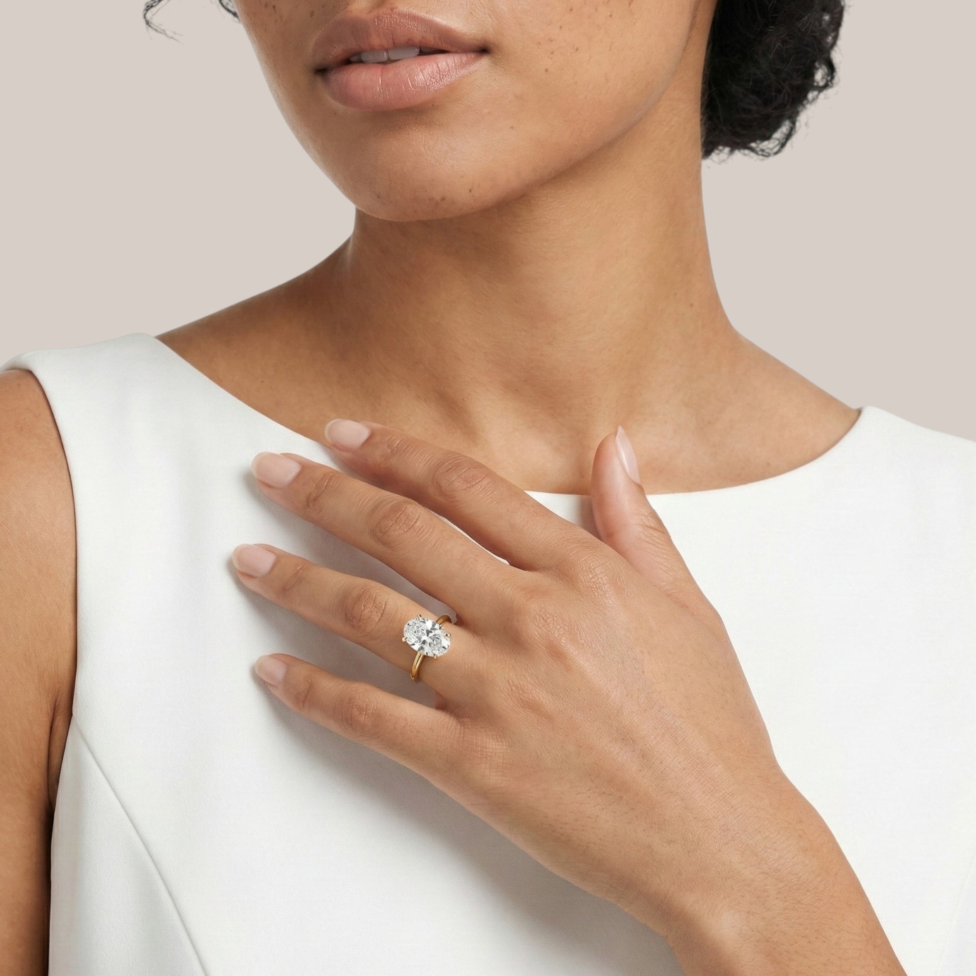 Woman wearing a gold ring with a diamond on a plain background