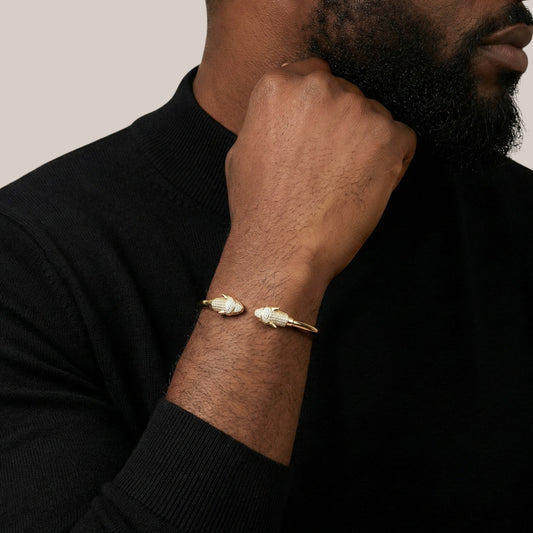 Man wearing a gold bracelet on his wrist with a neutral background
