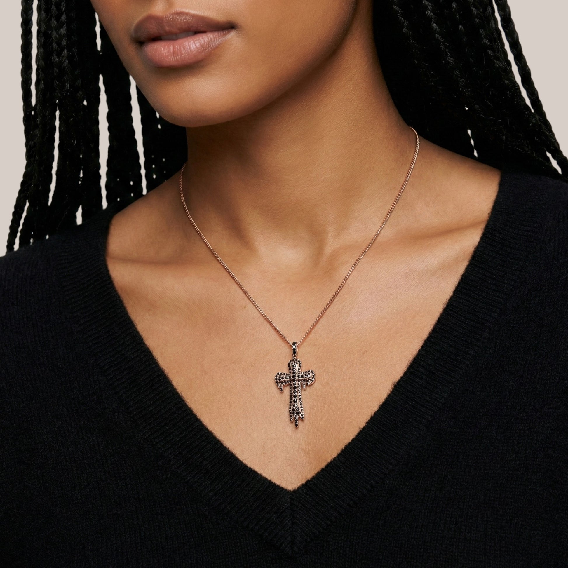 Close-up of a person wearing a necklace with a cross pendant against a neutral background
