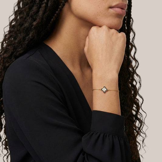 Woman wearing a gold bracelet with a clover charm on a neutral background