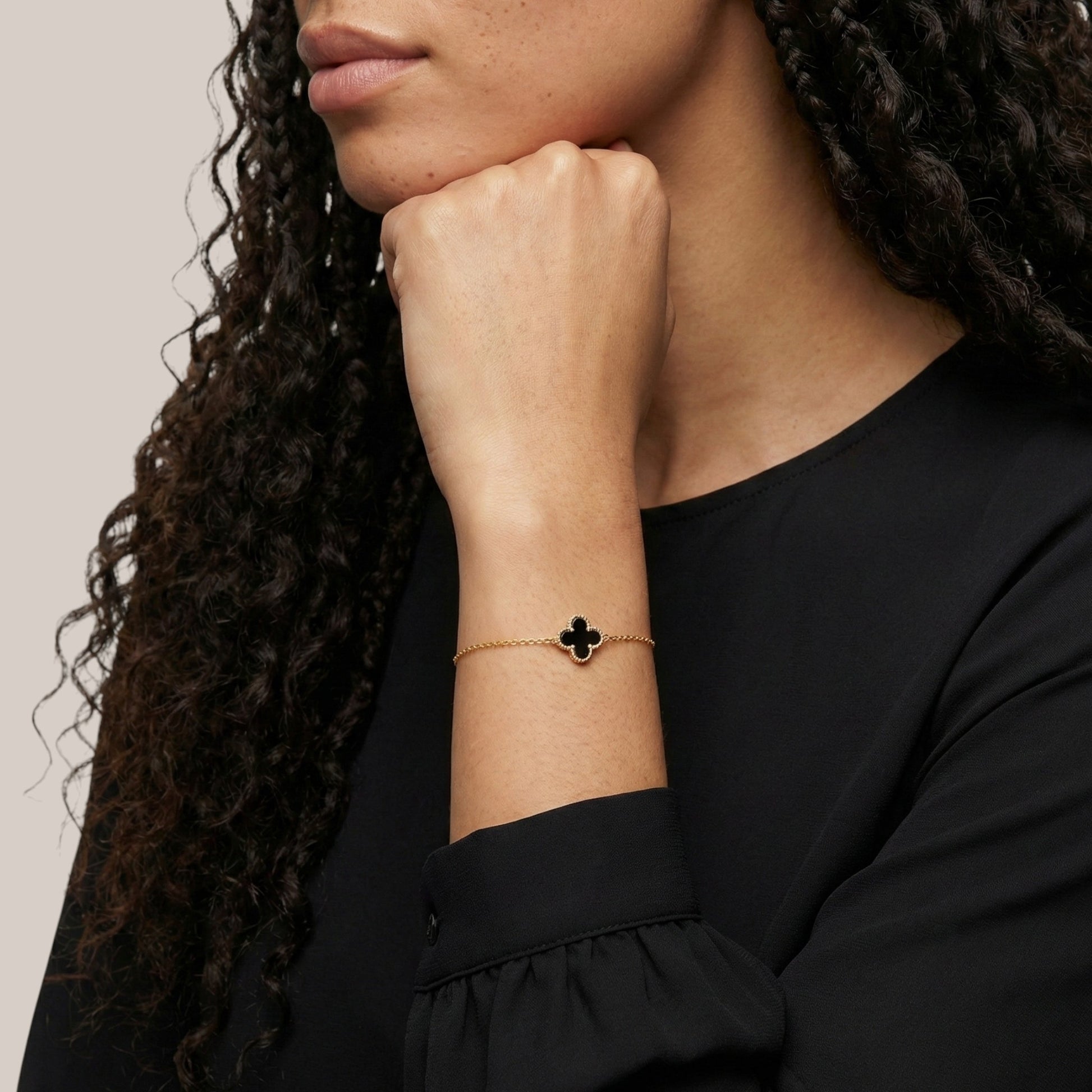Woman wearing a black clover bracelet on a neutral background