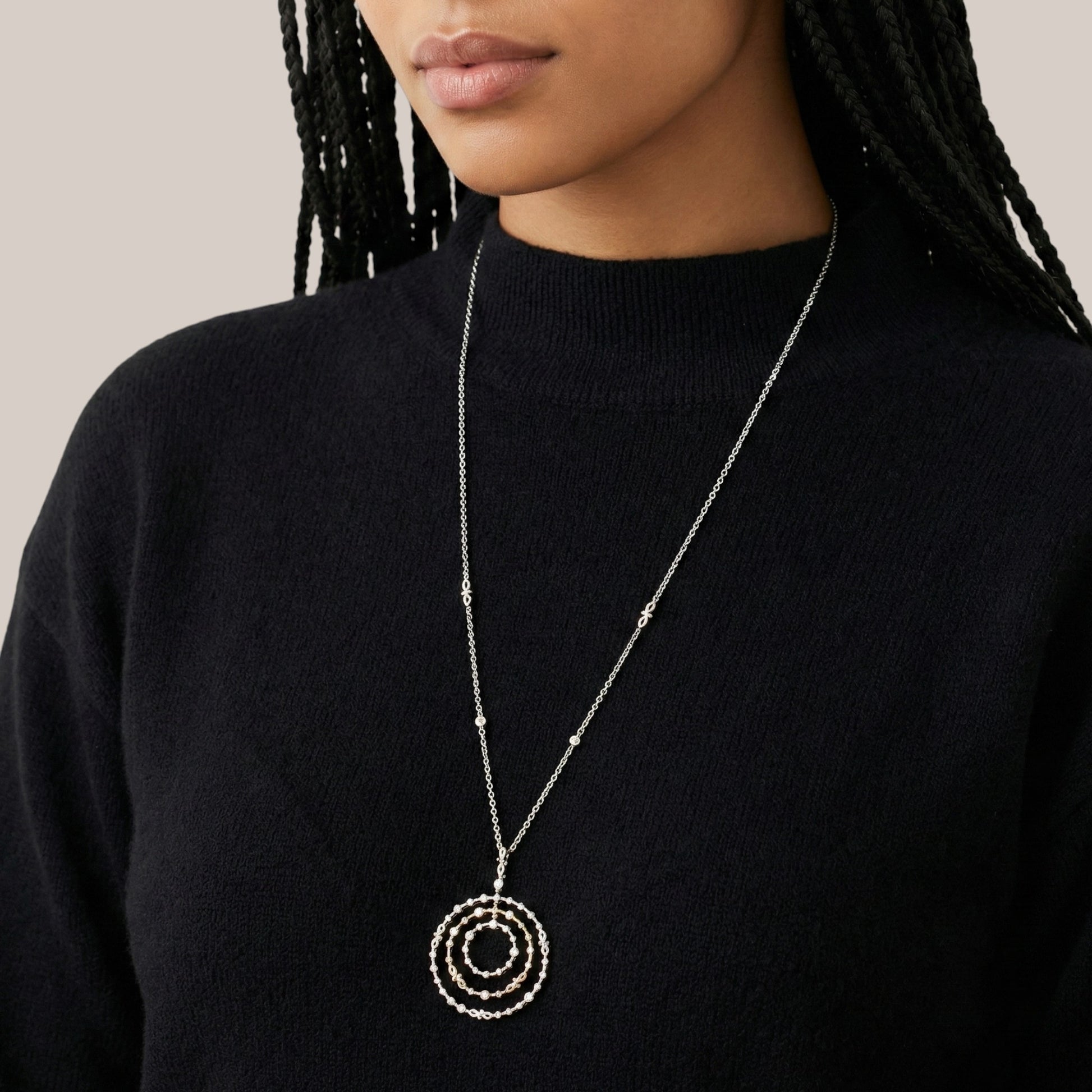 Person wearing a long necklace with a circular pendant on a plain background