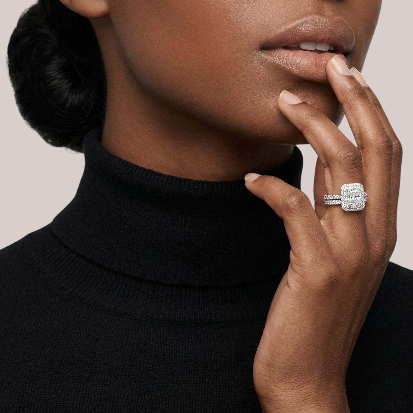 Woman wearing a black turtleneck with a diamond ring on her finger against a neutral background