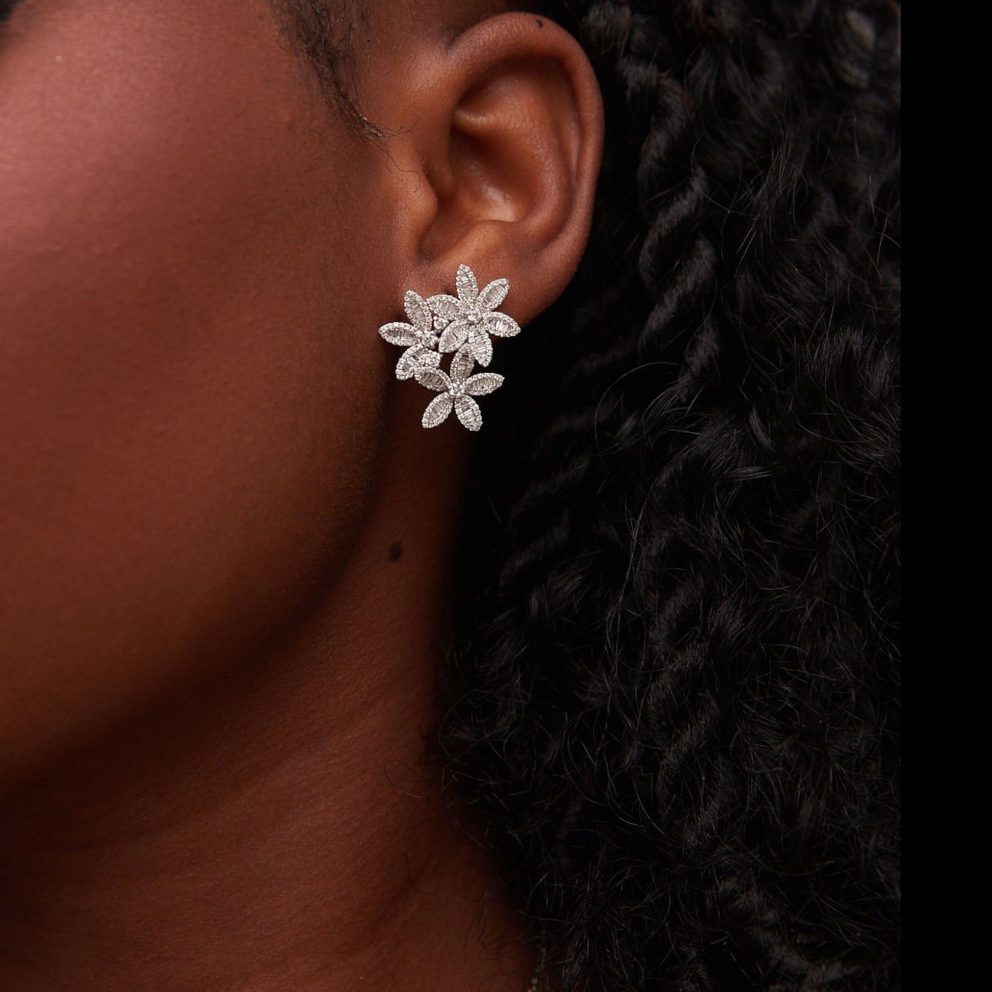 Close-up of an ear wearing a floral diamond earring with a dark background