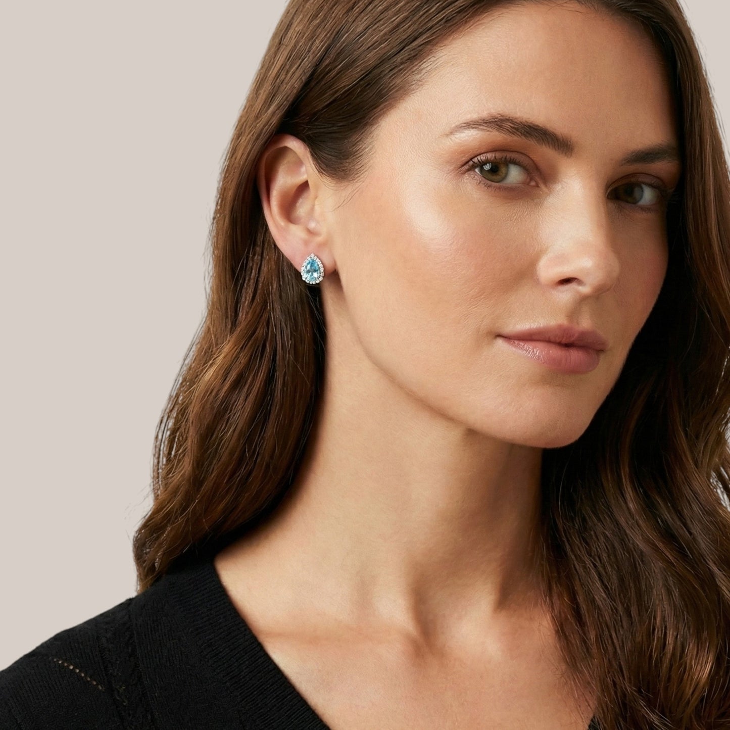 Woman wearing a blue gemstone earring against a neutral background