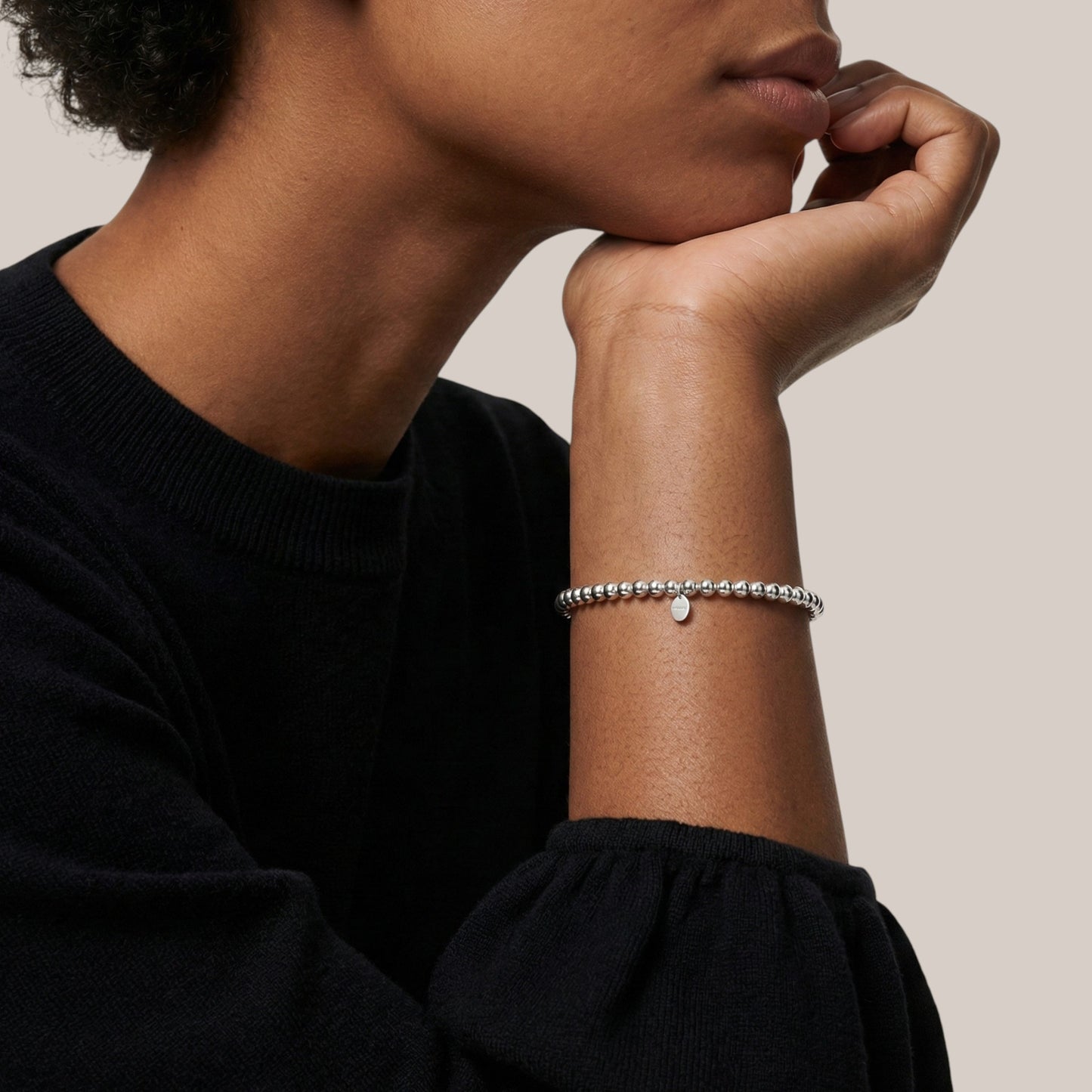 Person wearing a silver bracelet on a neutral background