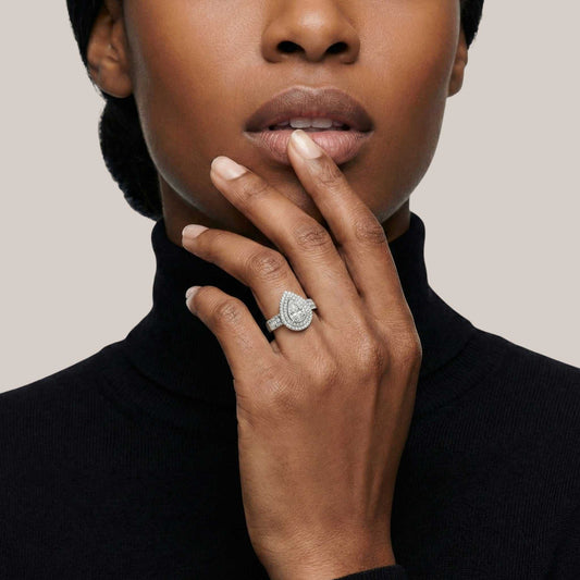 Person wearing a black turtleneck with a diamond ring on a neutral background