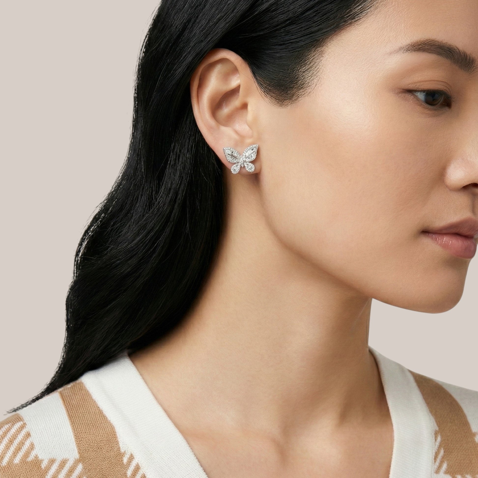 Close-up of a woman wearing butterfly-shaped earrings with a neutral background