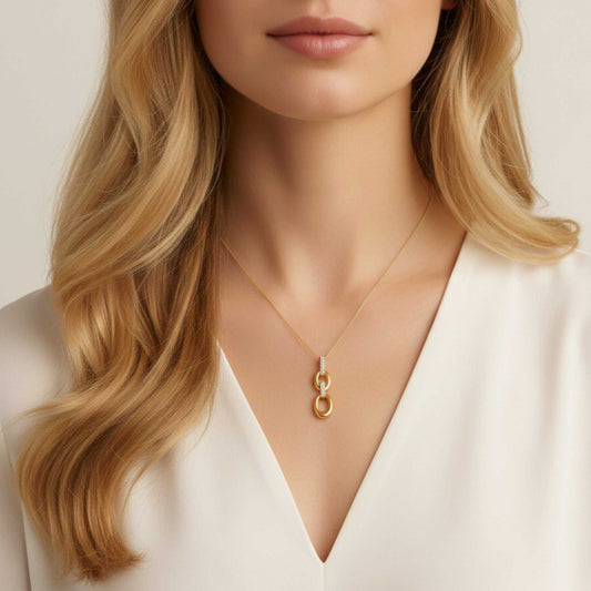 Close-up of a person wearing a gold necklace with a pendant against a neutral background