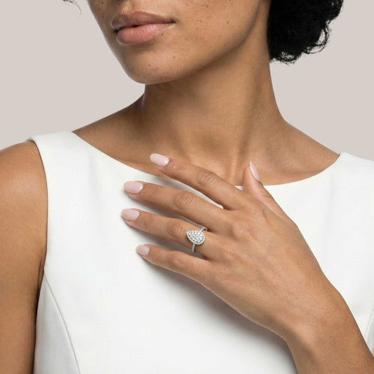 Woman wearing a silver ring with a heart-shaped diamond design on a plain background