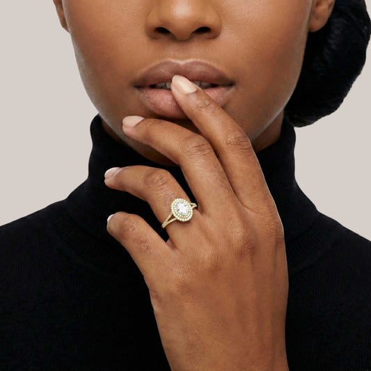 Person wearing a gold ring with a diamond on a plain background