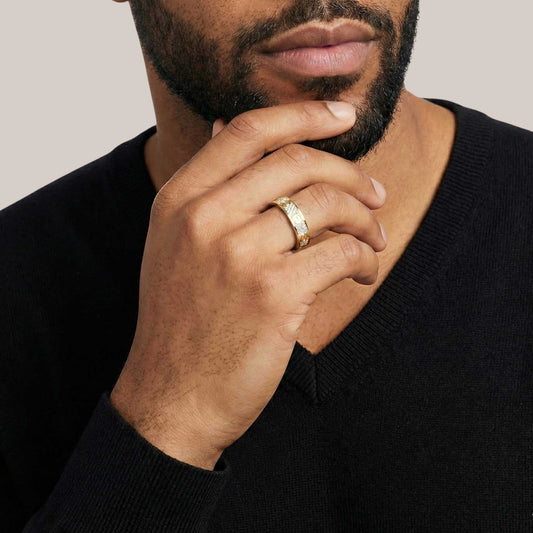 Man wearing a gold ring on his finger with a neutral background