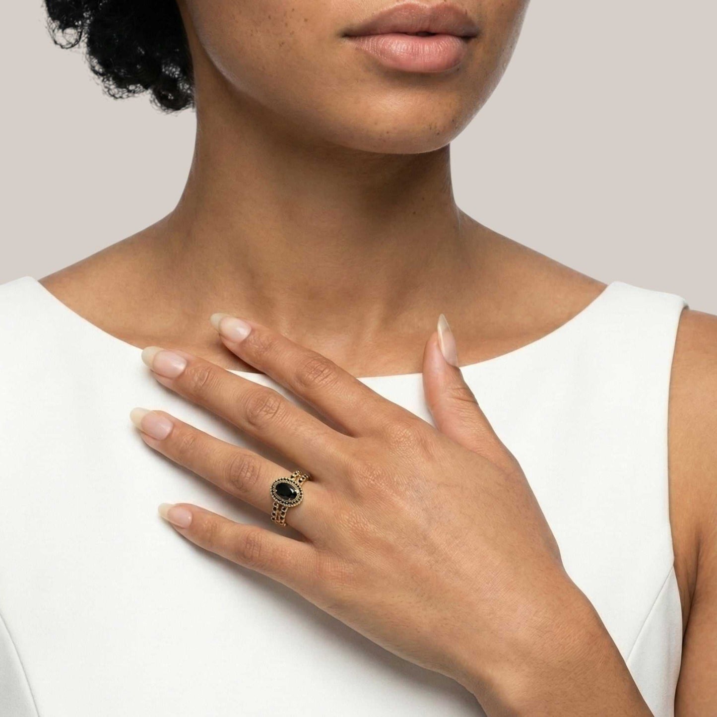 Close-up of a hand wearing a gold ring with a black stone, held against a plain background.