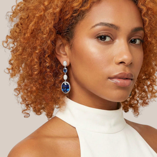 Woman wearing a pair of earrings with a white top against a neutral background