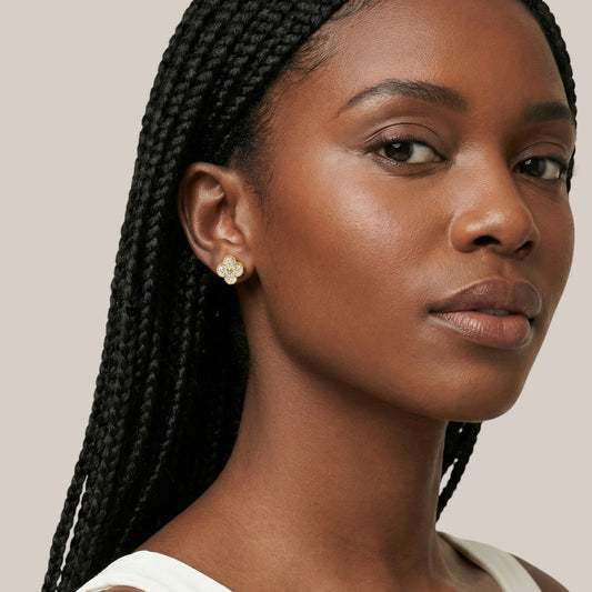 Woman with braided hair wearing a gold earring against a neutral background