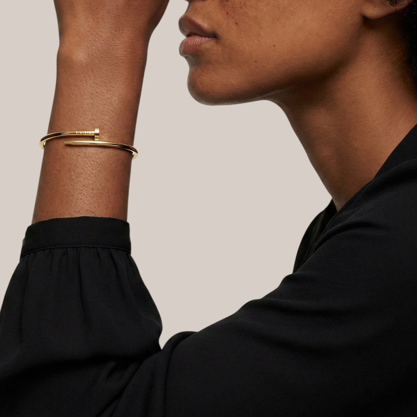 Close-up of a person wearing gold bracelets on a neutral background