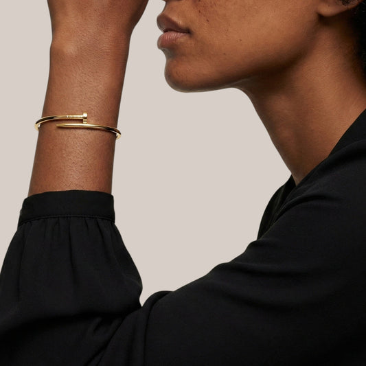 Close-up of a person wearing gold bracelets on a neutral background