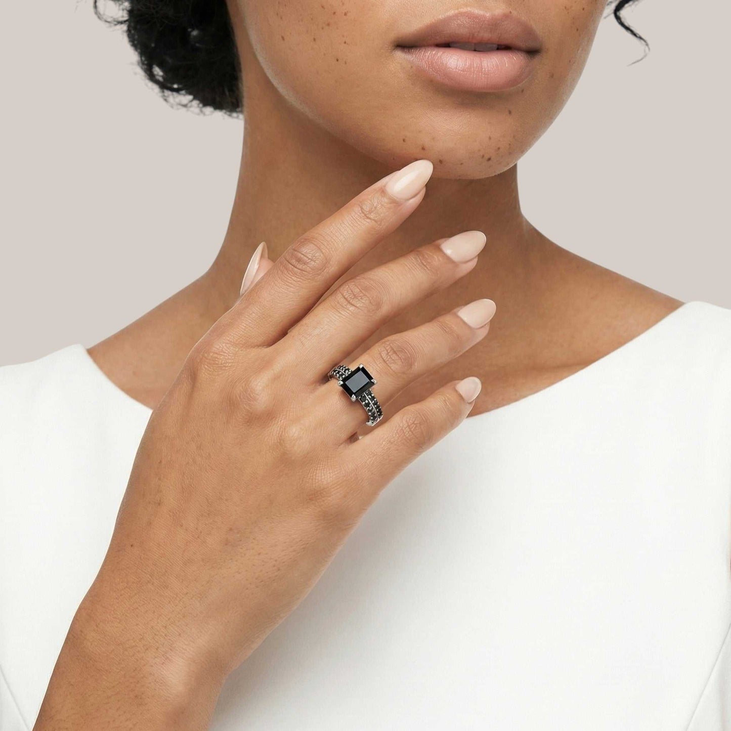Hand wearing a ring with a black gemstone on a neutral background