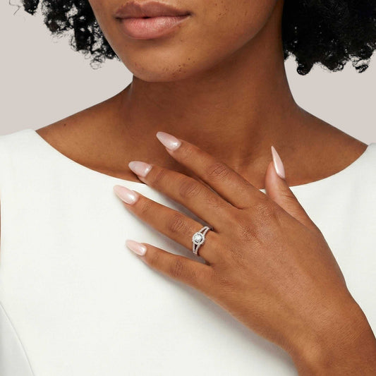 Close-up of a hand wearing a silver ring with a diamond, against a neutral background.