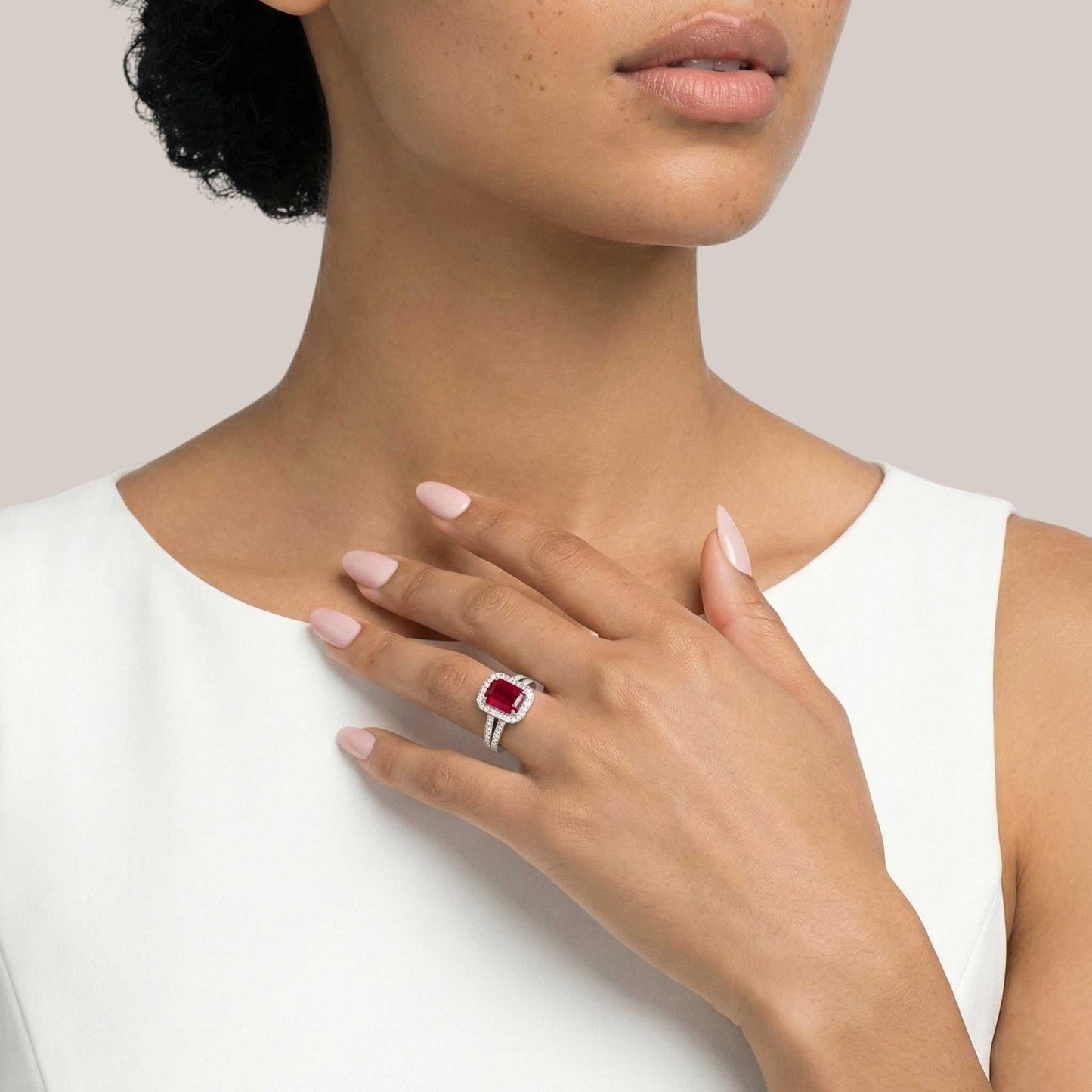 Close-up of a person wearing a ring with a red gemstone on a plain background