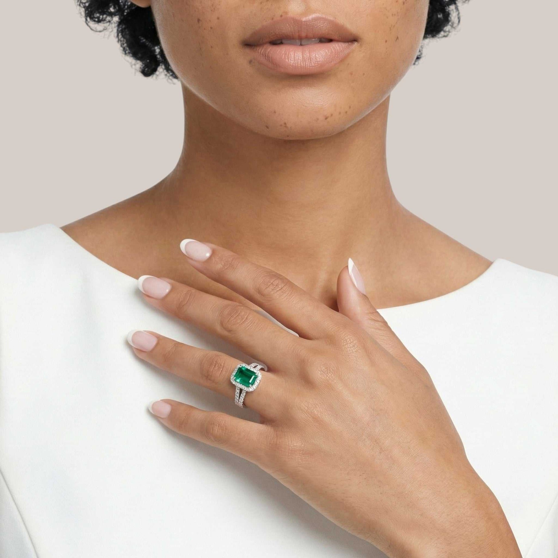 Hand wearing a green gemstone ring on a neutral background