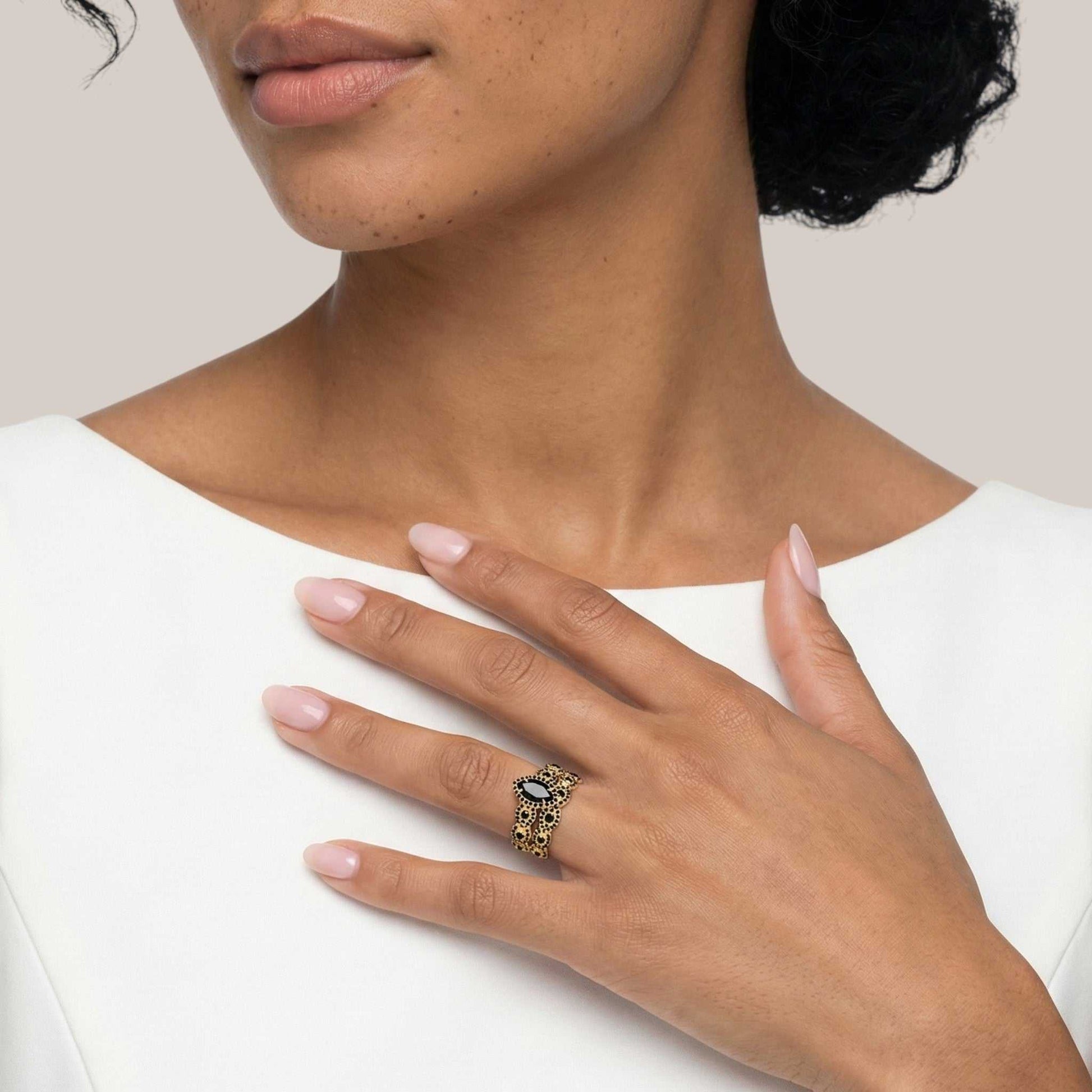 Close-up of a hand wearing a gold ring with a black stone, against a neutral background.