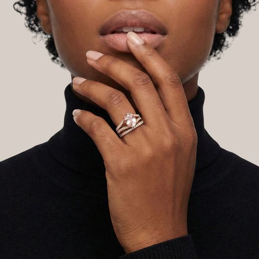 Close-up of a hand wearing a ring with a diamond, touching the chin against a neutral background