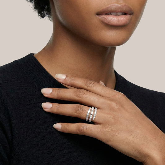 Close-up of a hand wearing multiple silver rings on a neutral background