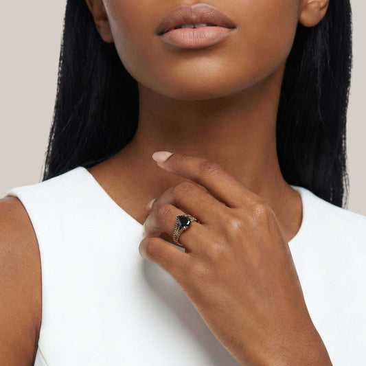 Close-up of a woman wearing a ring with a black gemstone on a plain background