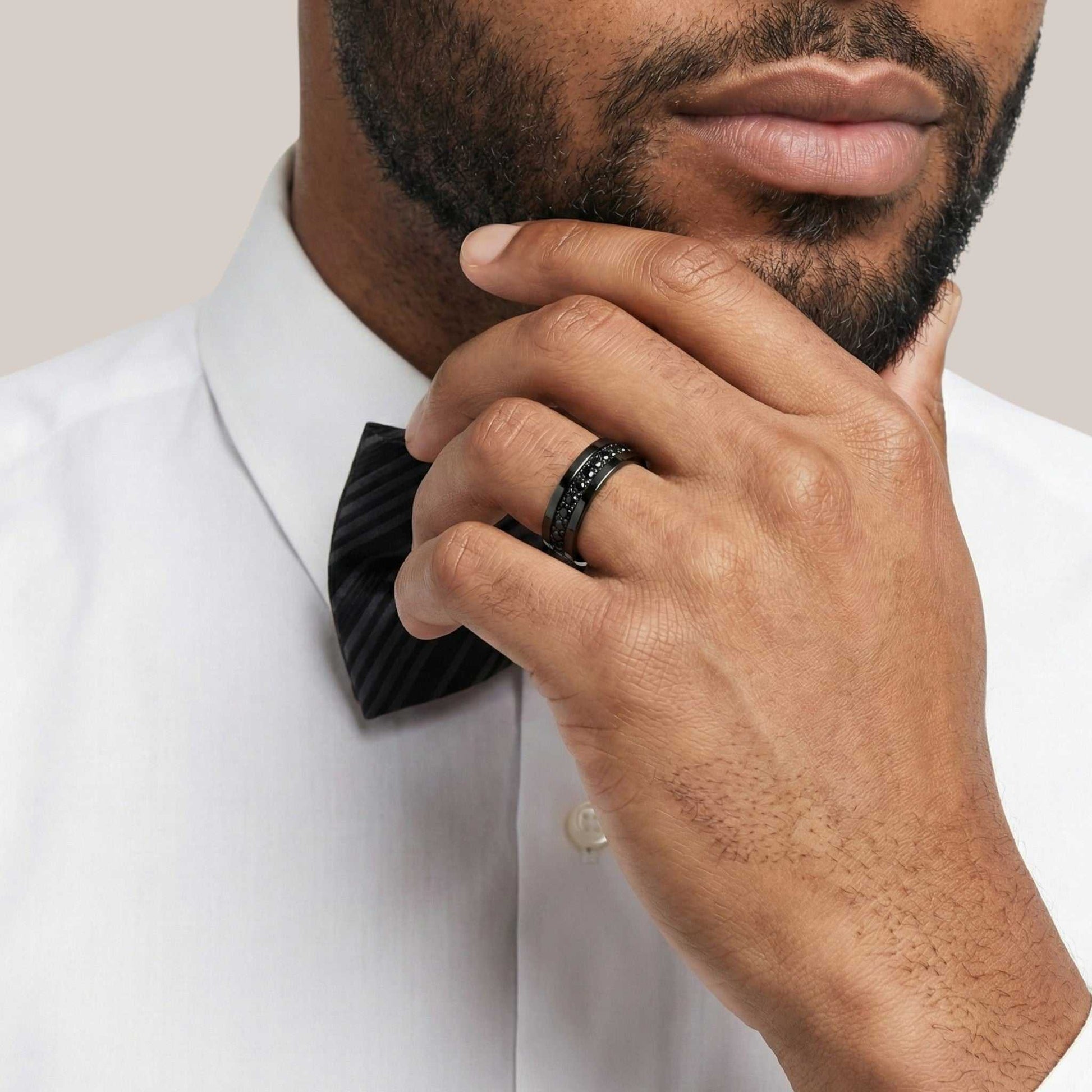 Man wearing a black bow tie and ring, with a neutral background