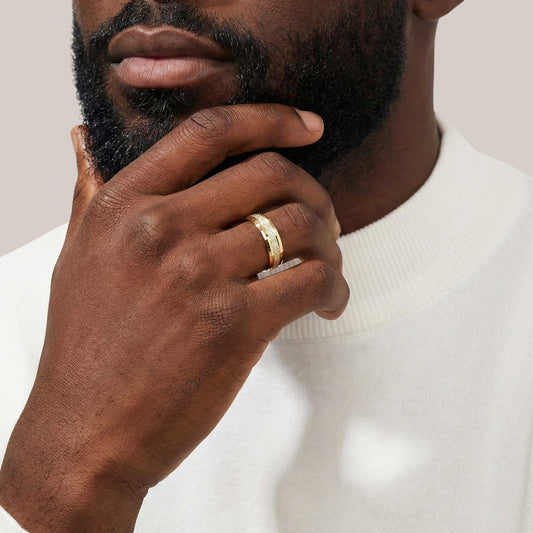 Man wearing a gold ring on his finger with a neutral background