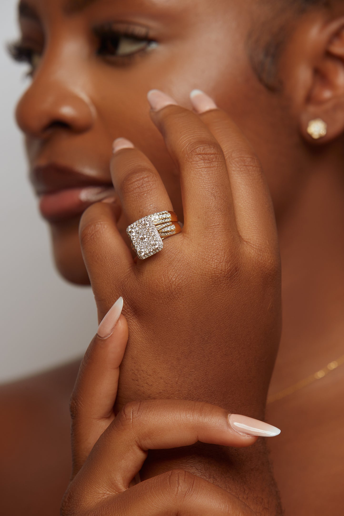 A close-up image of a woman's hand showcasing a radiant cut diamond ring with smaller diamonds around it, set in 18k gold.