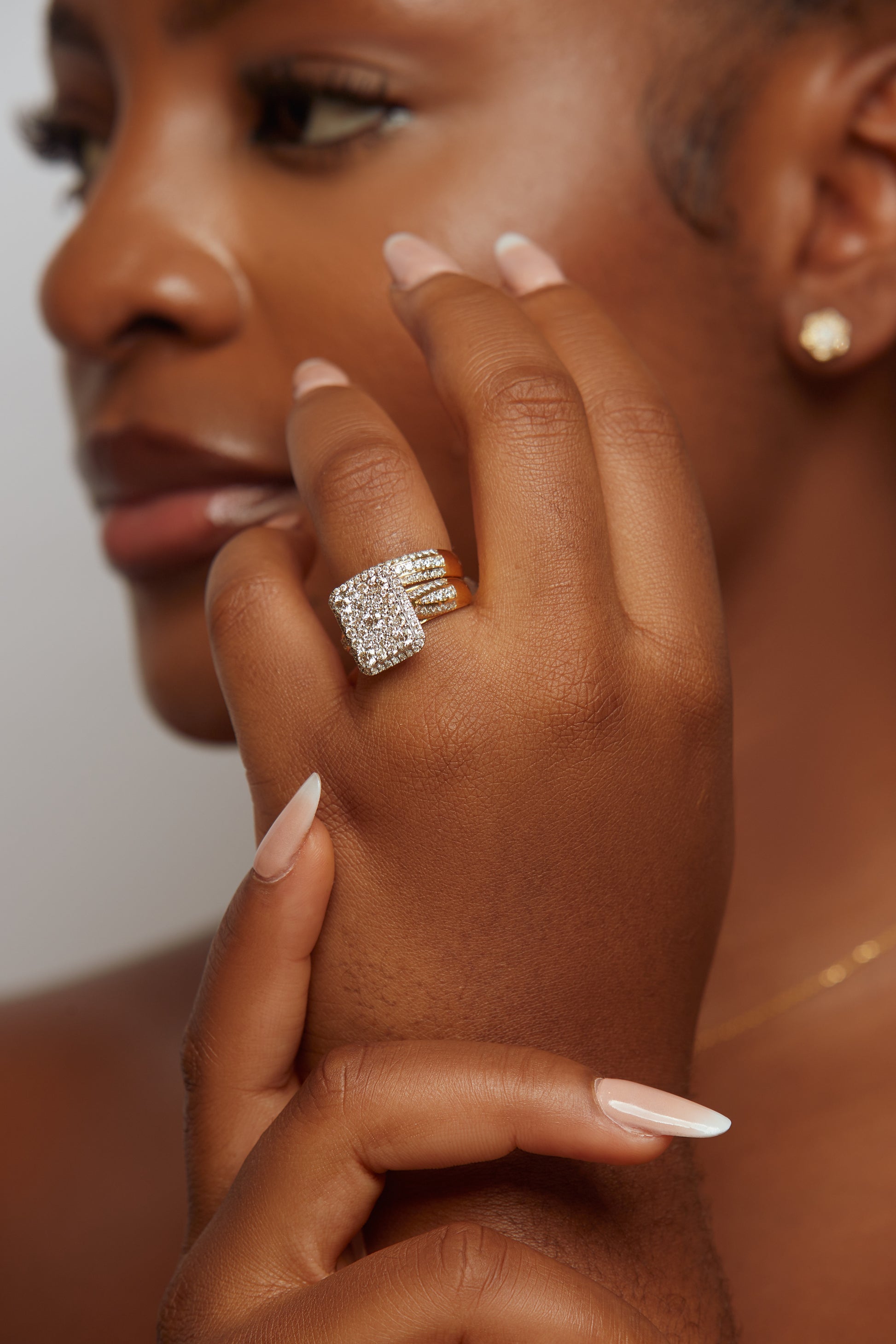 A close-up image of a woman's hand showcasing a radiant cut diamond ring with smaller diamonds around it, set in 18k gold.