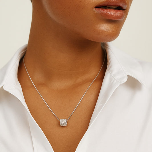 Silver necklace with a square pendant worn by a person in a white shirt.