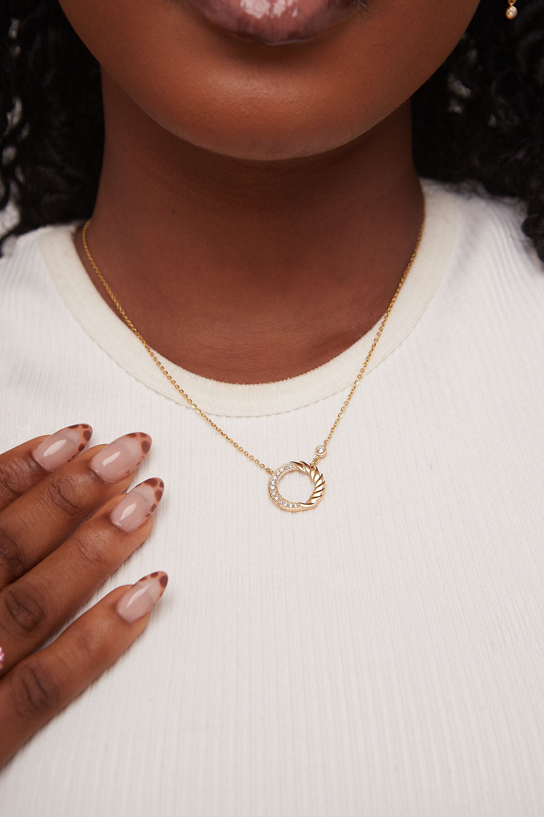 Gold necklace with a circular pendant worn by a person on a white background
