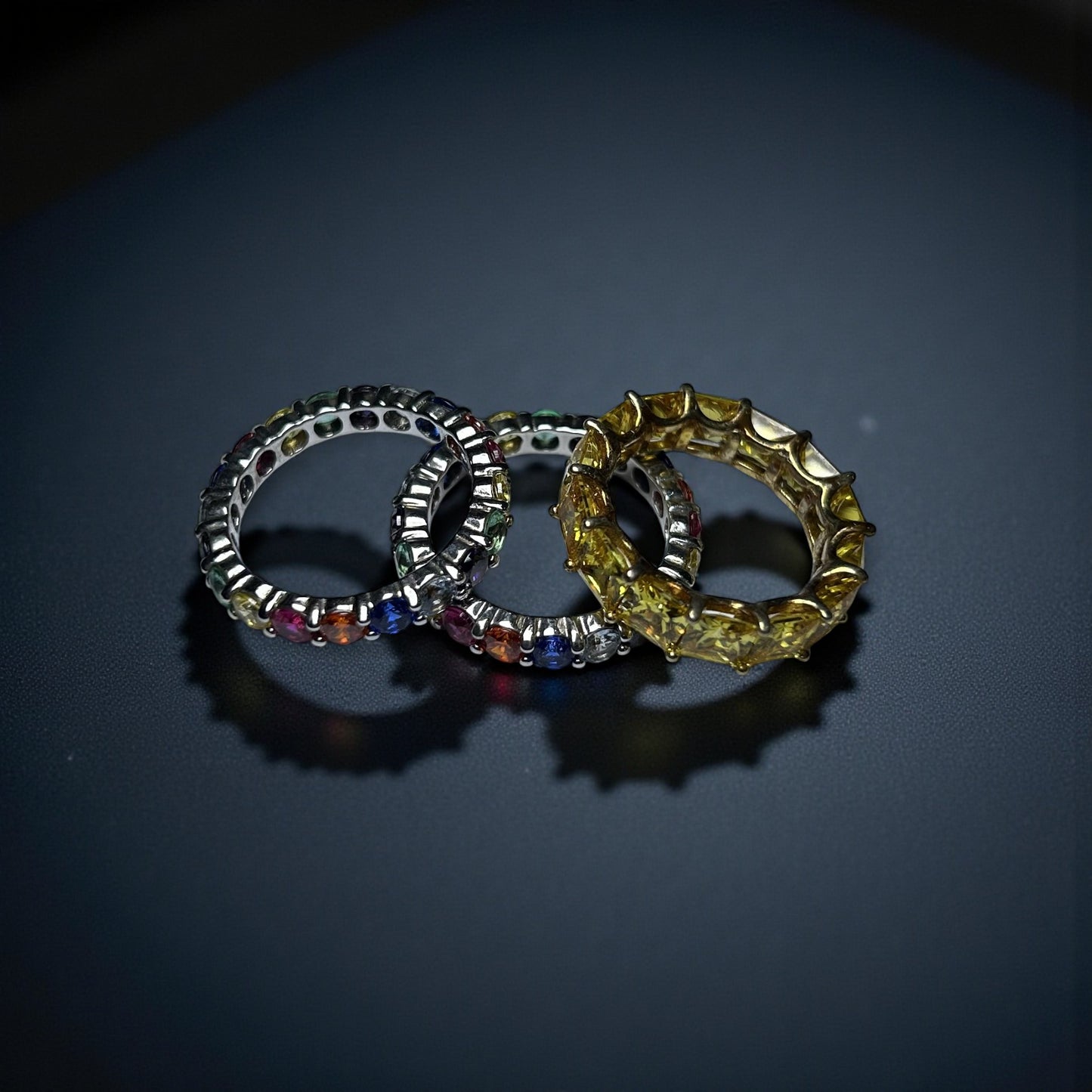 Three rings with colorful gemstones on a dark surface