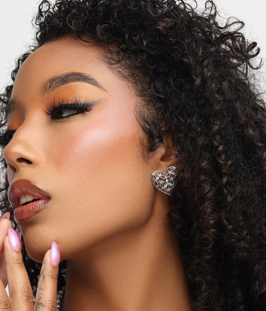Close-up of a woman with styled hair and makeup, wearing a silver heart-shaped earring.